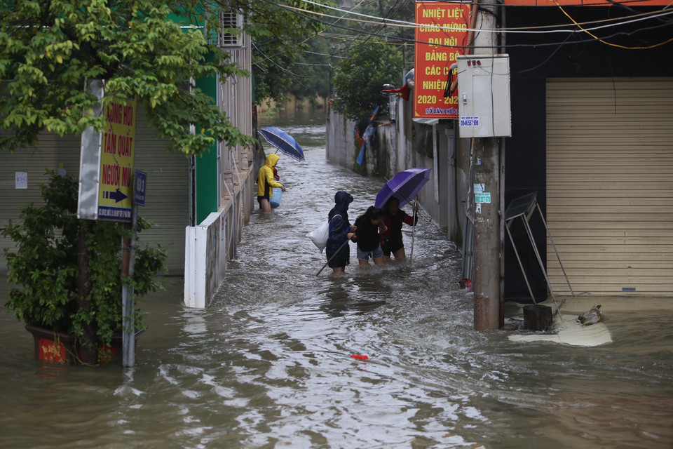 Người dân lội nước đi mua những nhu yếu phẩm cần thiết. (Ảnh: Hoàng Ngà/TTXVN)