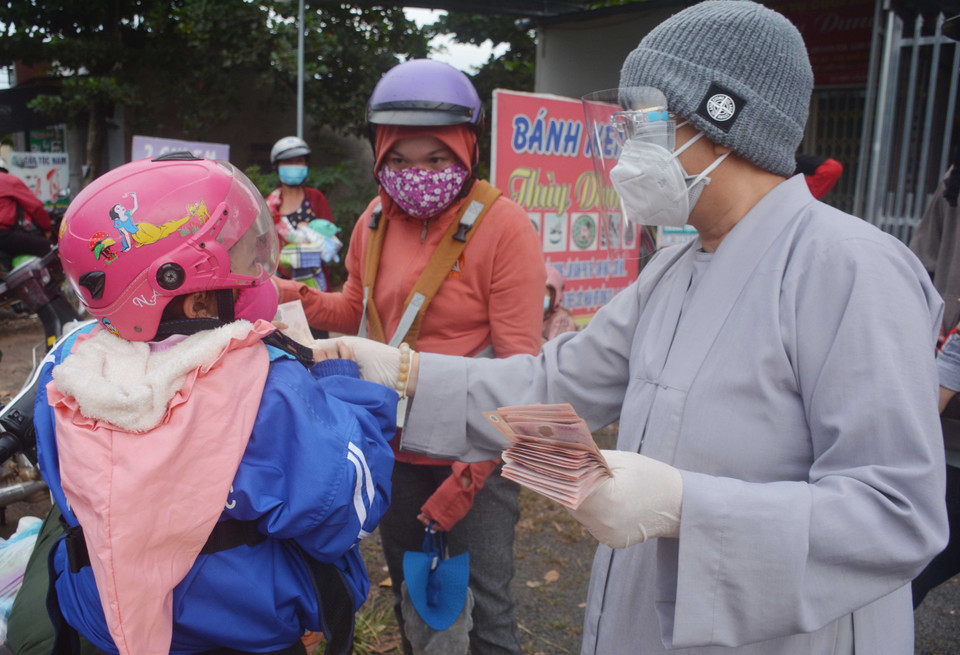 Đại diện chùa Thiên An (thành phố Buôn Ma Thuột) hỗ trợ tiền cho em nhỏ cùng cha mẹ về quê đi qua địa bàn tỉnh Đắk Lắk. (Ảnh: Hoài Thu/TTXVN)