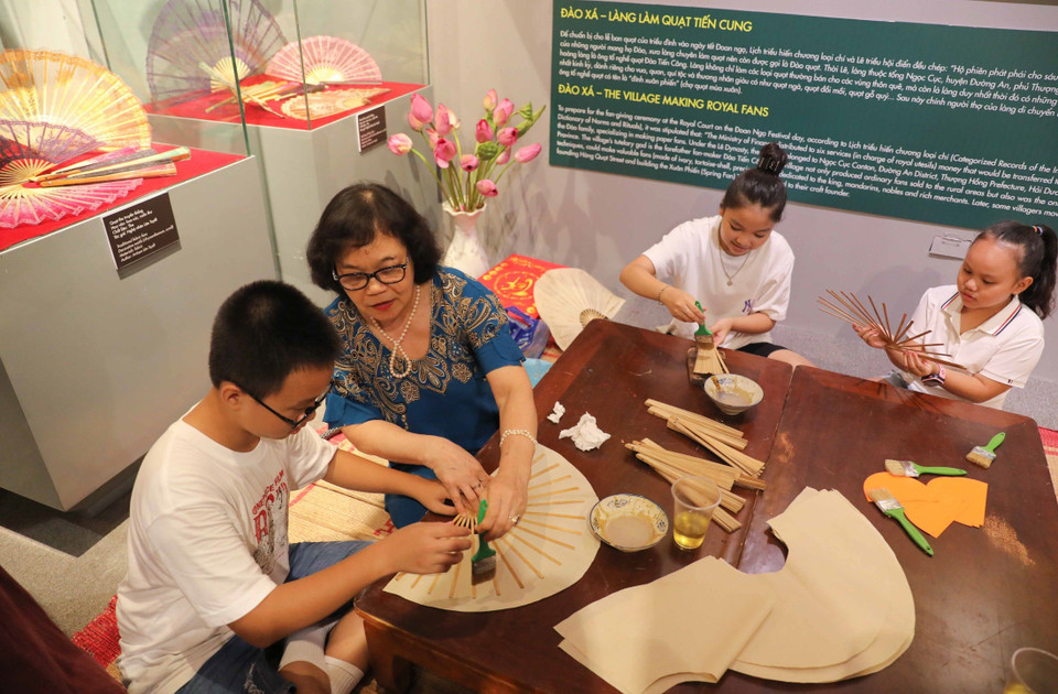 Nghệ nhân Nguyễn Lân Tuyết giới thiệu và hướng dẫn các em nhỏ làm quạt giấy truyền thống. (Ảnh: Thanh Tùng/TTXVN)