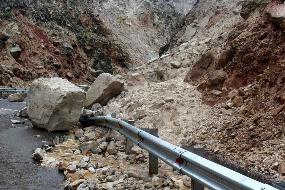 Hệ thống rãnh dọc thoát nước, hộ lan và mặt đường bị hư hỏng nặng do bị đất đá đè vào. (Ảnh: Công Tuyên/TTXVN)