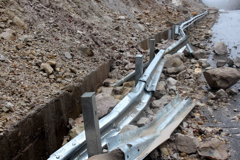 Hệ thống rãnh dọc thoát nước, hộ lan và mặt đường bị hư hỏng nặng do bị đất đá đè vào. (Ảnh: Công Tuyên/TTXVN)