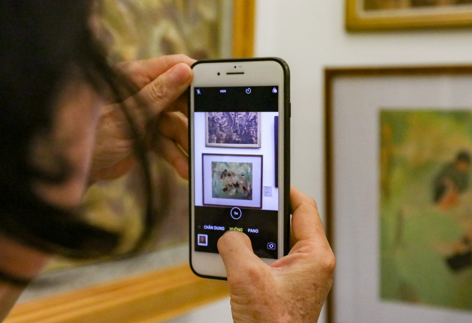 Một khách thăm quan dùng điện thoại chụp lại các bức tranh tại triển lãm. (Ảnh: Minh Hiếu/Vietnam+)