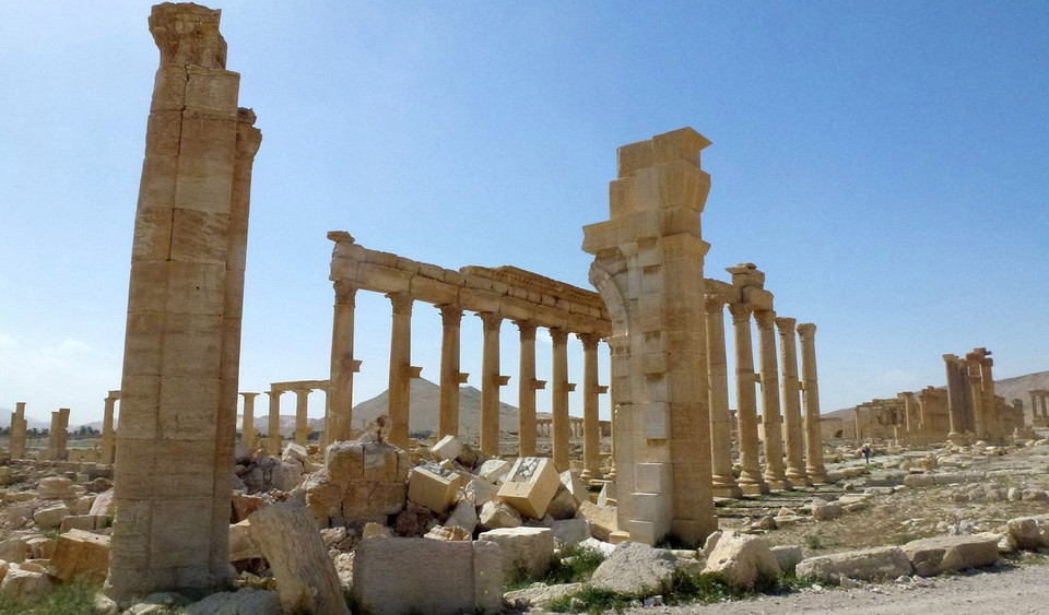 Palmyra nằm ở phía đông tỉnh Homs, là di sản thế giới được UNESCO công nhận, nơi lưu giữ nhiều di tích cổ và được coi là một trong những trung tâm văn hóa quan trọng của thế giới cổ đại. Sau khi chiếm giữ Palmyra, các tay súng của "Nhà nước Hồi giáo" (IS) tự xưng đã phá hủy một nhà tù quân sự và một số lăng mộ cổ ở đây. Trong ảnh: Khu tượng đài Arc de Triomph ở thành phố cổ Palmyra của Syria bị IS tàn phá, tháng 10/2015. (Ảnh: AFP/ TTXVN)