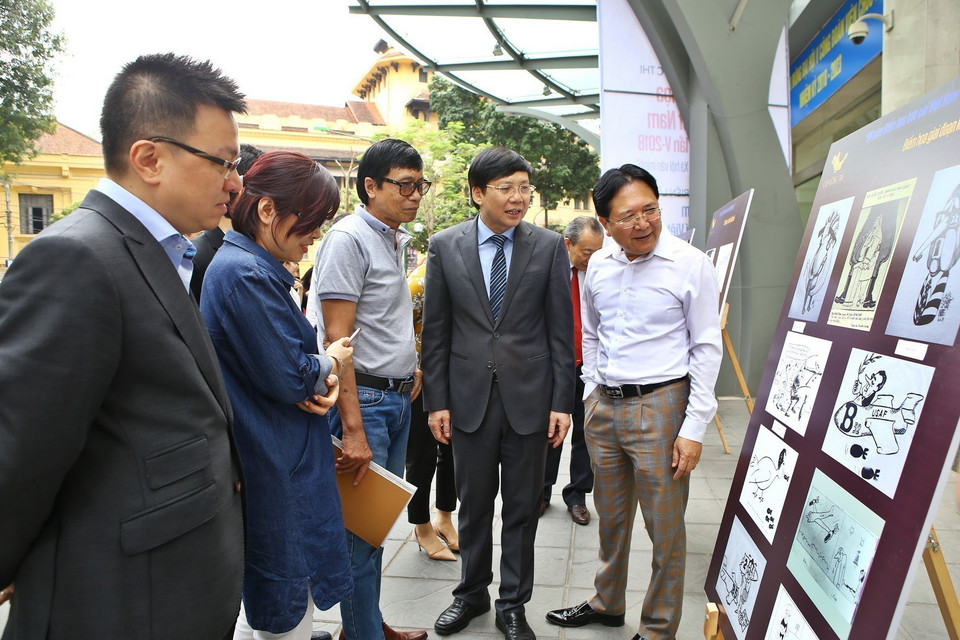 Phó Tổng giám đốc TTXVN Lê Quốc Minh (bên trái), Phó Chủ tịch Thường trực Hội Nhà báo Việt Nam Hồ Quang Lợi (thứ hai từ phải sang) và các đại biểu tham quan Triển lãm “96 năm biếm họa báo chí Việt Nam” sáng 3/4. (Ảnh: Minh Quyết/TTXVN)