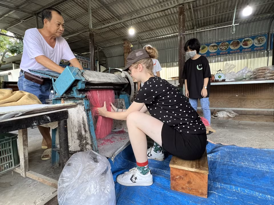 Du khách nước ngoài thích thú trải nghiệm quy trình sản xuất hủ tiếu đa sắc. (Ảnh: TTXVN phát)