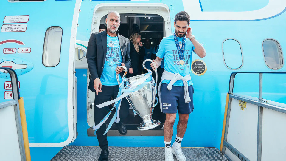 HLV Pep Guardiola và thủ quân Ilkay Gundogan cầm cúp rời máy bay khi về đến Anh. (Nguồn: Man City)