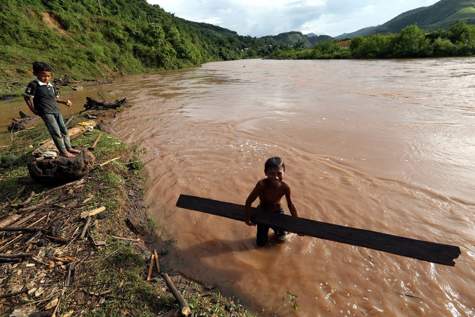 Một cậu bé vớt được thanh củi to trôi dưới sông. (Ảnh: Phan Tuấn Anh/TTXVN)