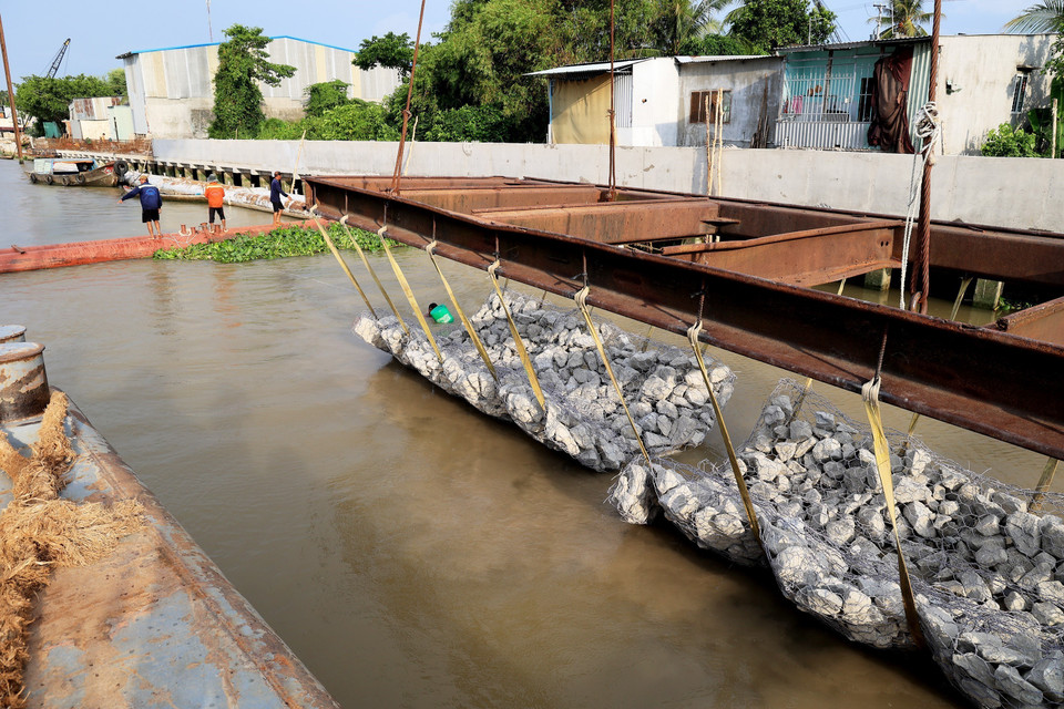Hạ thủy giằng đá xuống bãi địa dưới lòng sông để làm kè chống sạt lở bờ sông Tiền. (Ảnh: Hồng Đạt/TTXVN)