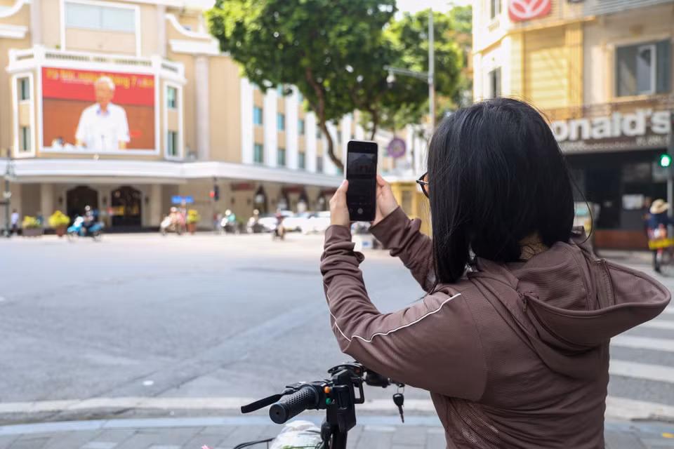 Một người dân đang đứng ghi lại hình ảnh của Tổng Bí thư Nguyễn Phú Trọng trên màn hình LED của một trung tâm thương mại phố Tràng Tiền. (Ảnh: Minh Hiếu/Vietnam+)