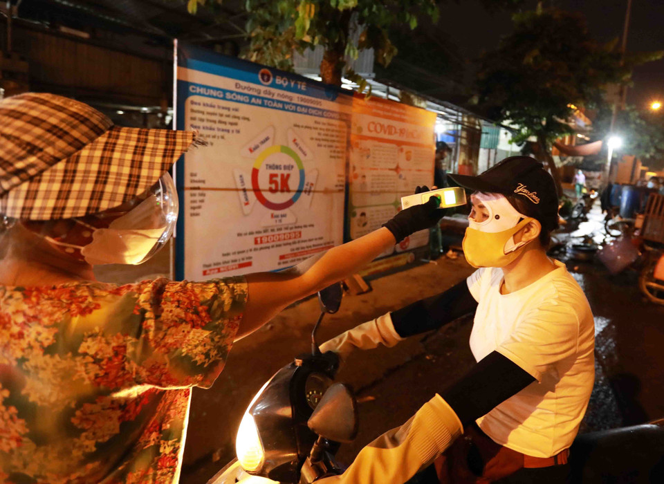 Ban quản lý chợ đo thân nhiệt cho tất cả người dân khi đến chợ để phòng, chống dịch. (Ảnh: Vũ Sinh/TTXVN)