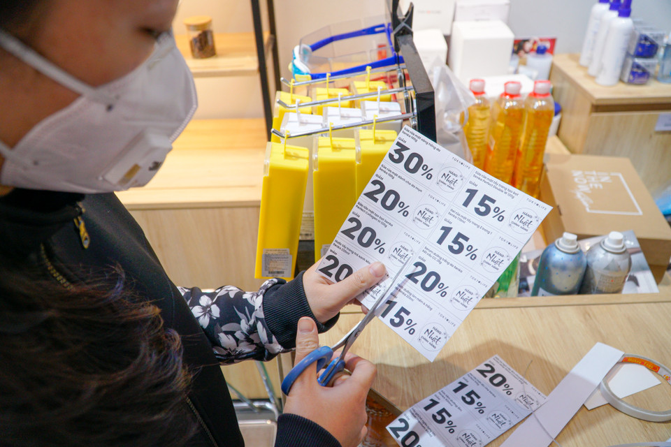 Nhân viên cửa hàng cửa hàng bán lẻ đồ đa dụng Tokyolife phố Chùa Bộc đang dán nhãn giảm giá cho các sản phẩm. (Ảnh: Minh Hiếu/Vietnam+)