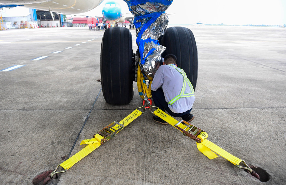 Các kỹ sư của Công ty Trách nhiệm hữu hạn Một thành viên Kỹ thuật máy bay (VAECO) cố định dây, bọc kín các bộ phận quan trọng của máy bay trước khi bão số 3 đổ bộ vào Miền Bắc. (Ảnh: PV/Vietnam+)