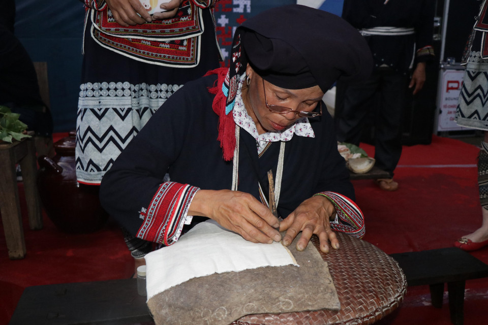 Nghệ nhân người Dao trình diễn in hoa văn bằng sáp ong. (Ảnh: Hữu Quyết/TTXVN)