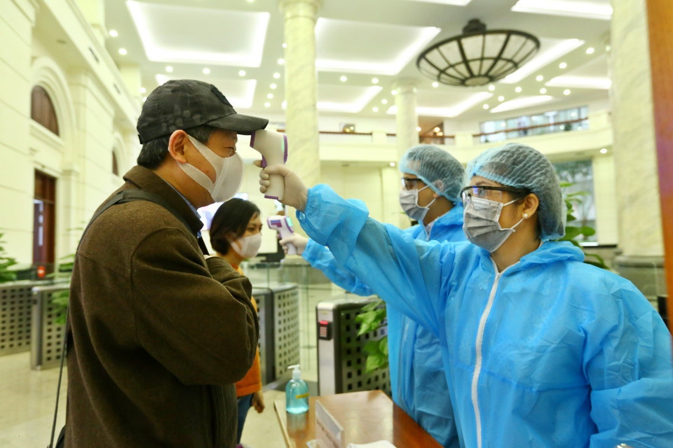 Cán bộ, nhân viên cơ quan Bộ Tài chính được bộ phận lễ tân đo thân nhiệt trước khi vào cơ quan. (Ảnh: Minh Quyết/TTXVN)