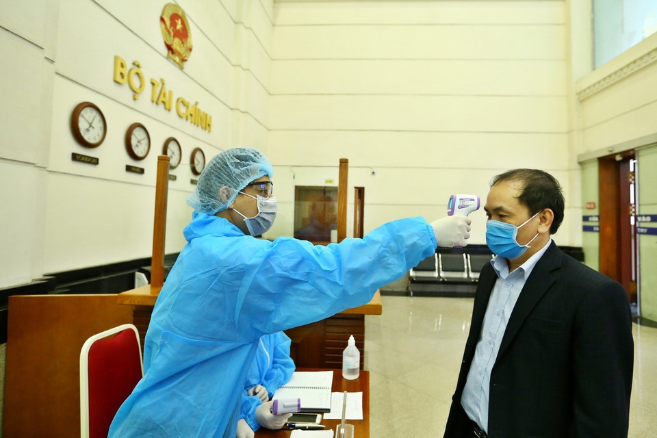 Cán bộ, nhân viên cơ quan Bộ Tài chính được bộ phận lễ tân đo thân nhiệt trước khi vào cơ quan. (Ảnh: Minh Quyết/TTXVN)