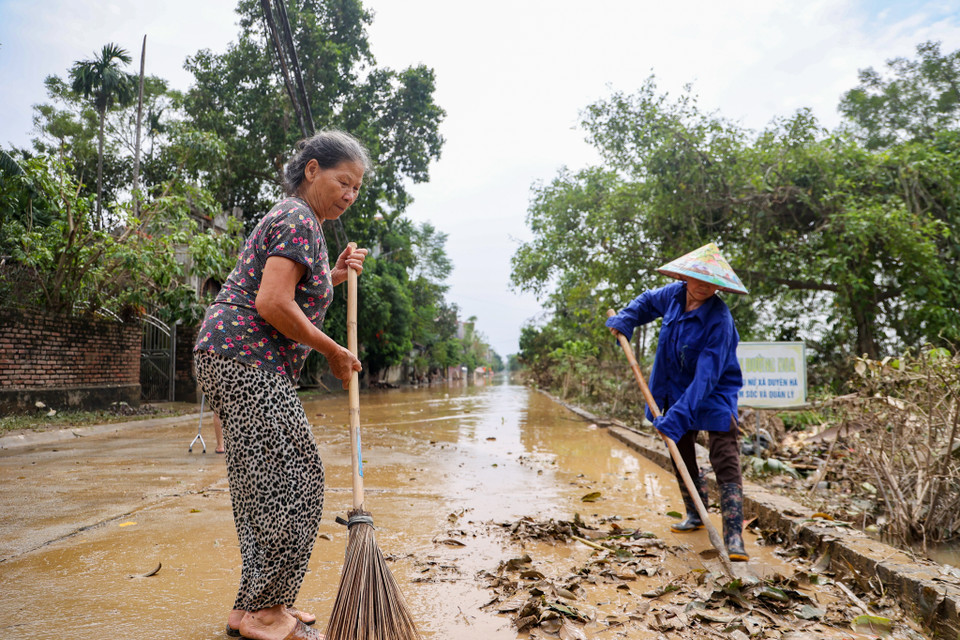 Bà Phạm Thị Thái, người dân thuộc Đội 4, thôn Đại Lan đang cùng bà con trong làng quét dọn đường sá để lấy lối đi lại. Bà Thái cho biết từ sáng sớm nay nước rút rất nhanh, đến nay khu vực từ ngoài cổng làng đến đoạn đầu làng gần như đã rút hết. "Tôi cũng mong nước mau chóng rút nhanh để người dân chúng tôi có thể ổn định lại cuộc sống," bà Thái nói thêm. (Ảnh: Minh Hiếu/Vietnam+)