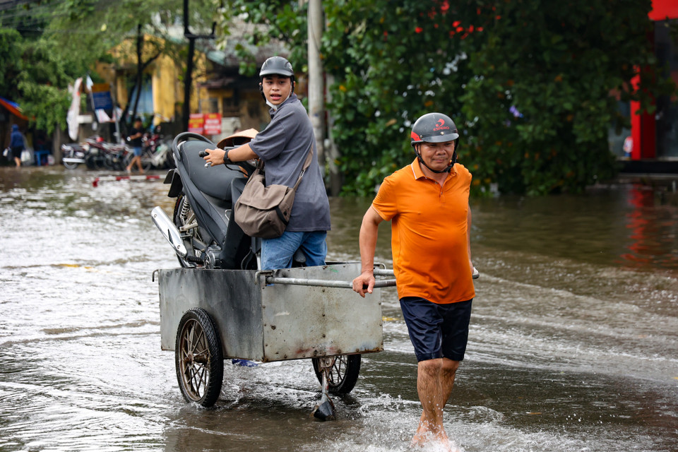 Bởi lượng nước ngập sâu không thể di chuyển, một số người đã tranh thủ làm dịch vụ kéo xe máy qua khu vực ngập. (Ảnh: Minh Hiếu/Vietnam+)