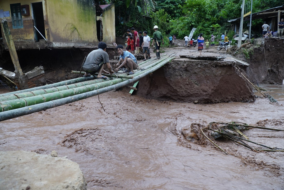 Người dân làm cầu tạm để đi sau khi bị nước lũ cuốn trôi mất đường. (Ảnh: Xuân Tư/TTXVN)