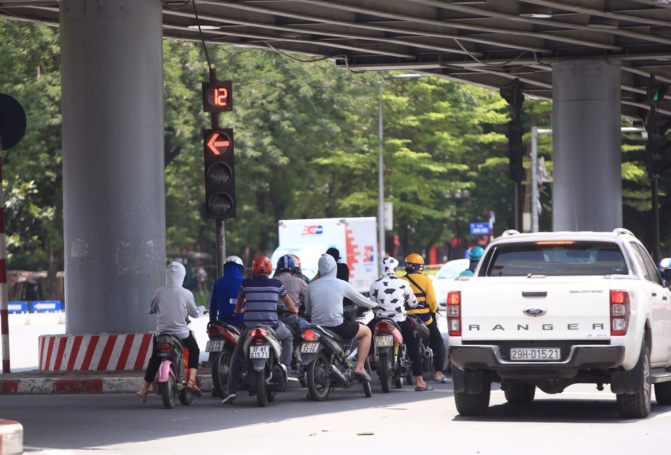 Những người tham gia giao thông chọn chỗ có bóng râm tránh nắng, nóng gay gắt khi chờ đèn đỏ (chụp lúc 11h30 ngày 28/5 tại ngã tư Thái Hà-Chùa Bộc). (Ảnh: Hoàng Hiếu/TTXVN)