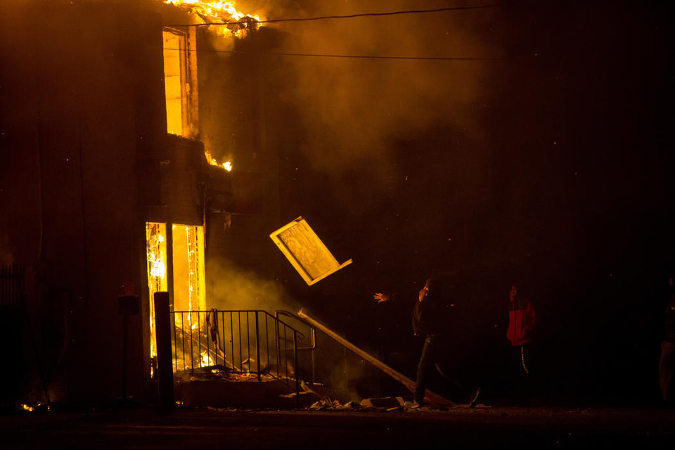 Một người biểu tình ném gỗ vào một kho chứa hàng đang cháy ngày 24/11 ở Ferguson, Missouri. (Nguồn: AP)