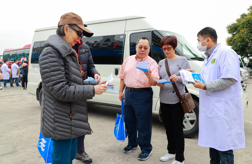 Ngay khi xuống xe để vào thăm quan vịnh Hạ Long (Quảng Ninh) khách du lịch được phát tờ rơi truyền thông về nCov. (Ảnh: TTXVN)