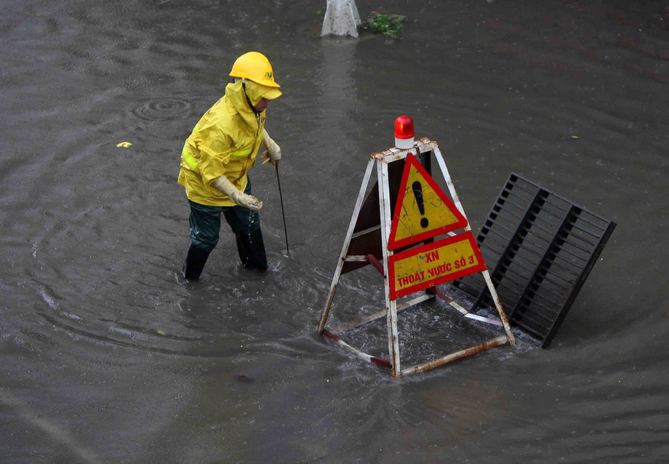 Công nhân Xí nghiệp thoát nước Hà Nội túc trực, cảnh báo người đi đường tại các điểm ngập nguy hiểm. (Ảnh: Thanh Tùng/TTXVN)
