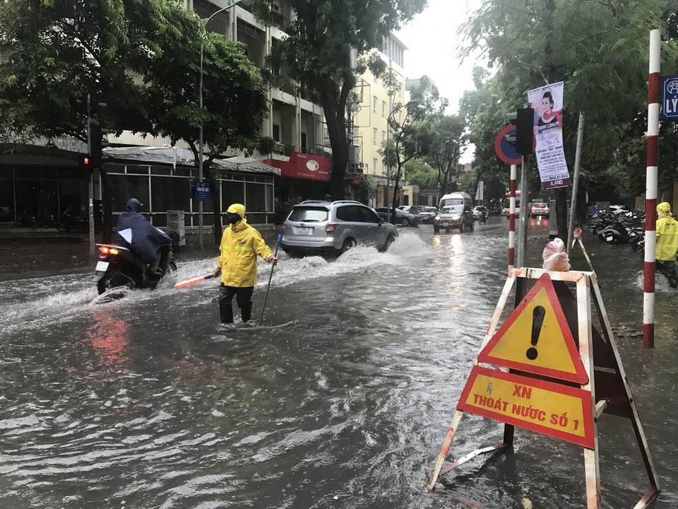 Nhân viên xí nghiệp thoát nước số 1 hướng dẫn người dân di chuyển qua chỗ nước ngập trên phố Phan Bội Châu (Hà Nội). (Ảnh: Minh Quyết/TTXVN)