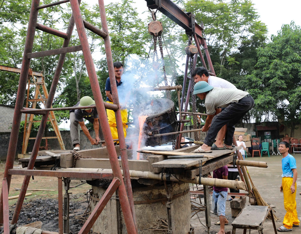 Các nghệ nhân thực hiện rót đồng vào khuôn trống. (Ảnh: Thanh Tùng/TTXVN)