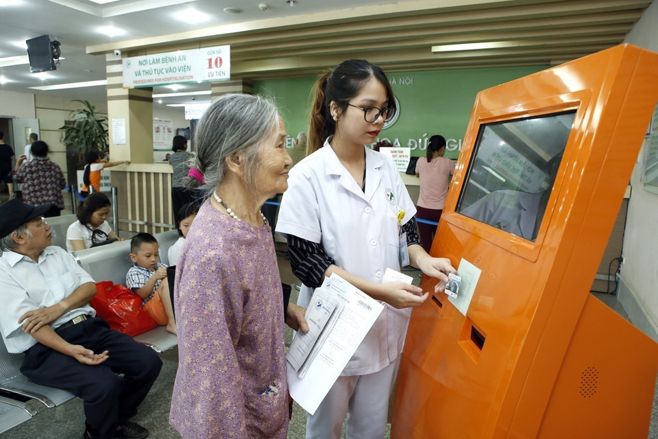 Để mọi người dân đều có khả năng tiếp cận với các dịch vụ y tế, chăm sóc sức khỏe có chất lượng ngay tại cơ sở, ngành y tế Hà Nội luôn củng cố, hoàn thiện và phát triển hệ thống y tế cơ sở, qua đó góp phần quan trọng vào thực hiện nhiệm vụ chăm sóc sức khỏe cho nhân dân.Trong ảnh: Nhân viên y tế hướng dẫn người bệnh thao tác, đặt thẻ quẹt máy tự động nhận và hiển thị thông tin cá nhân khám chữa bệnh tại bệnh viện Đa khoa Đức Giang. (Ảnh: Dương Ngọc/TTXVN)