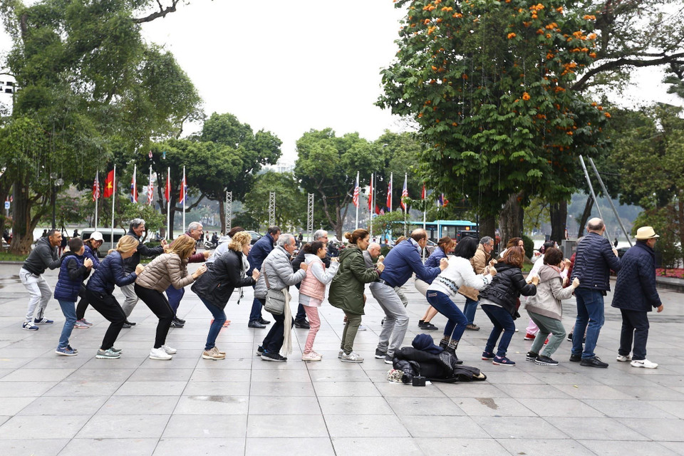 Đoàn khách du lịch quốc tế cùng tập thể dục với người dân Thủ đô tại khu vực vườn hoa Lý Thái Tổ bên hồ Hoàn Kiếm. (Ảnh: Minh Quyết/TTXVN)