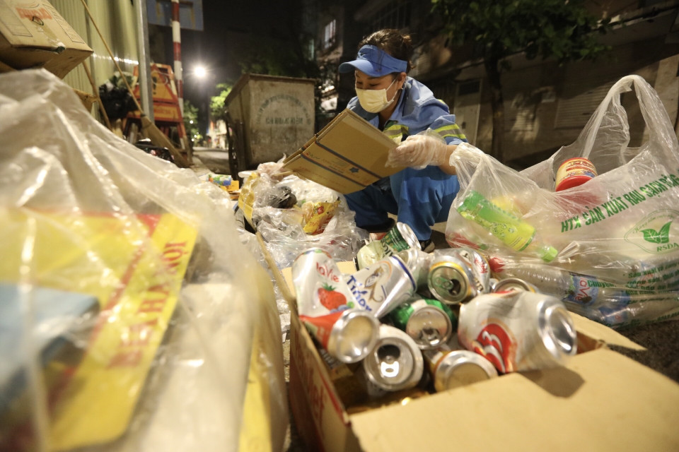 Người lao công tranh thủ thu gom những vỏ chai, lọ để bán đồng nát. (Ảnh: Minh Quyết/TTXVN)