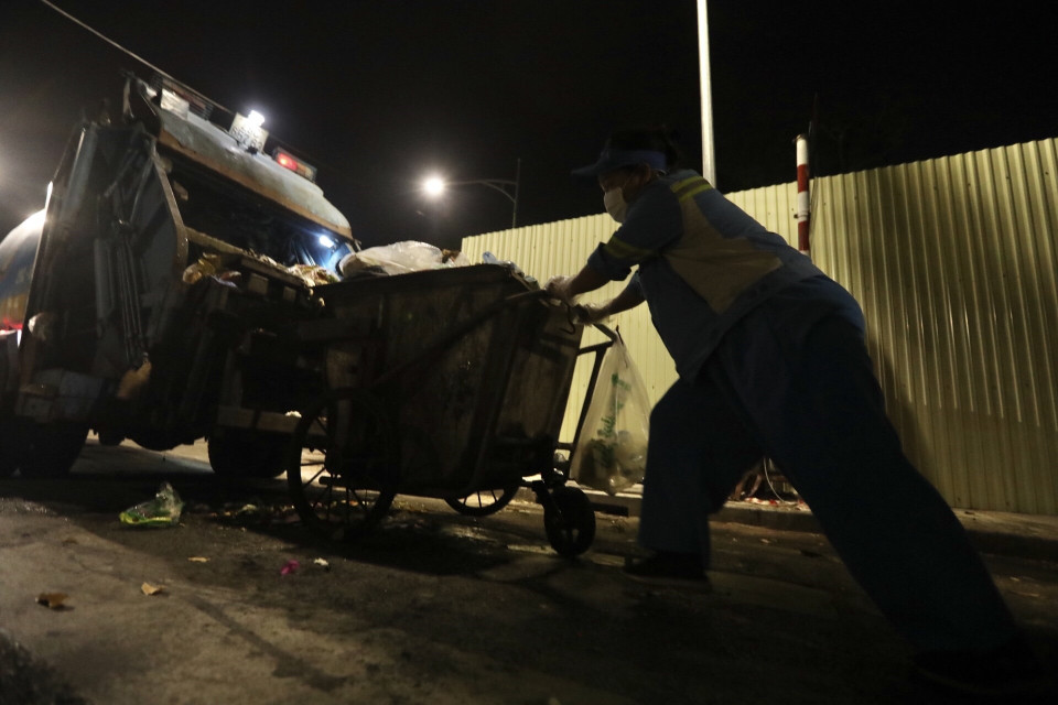 Khi xe chuyên dụng đến thu gom rác, người lao công nhanh chóng đẩy những xe rác đến thùng xe. (Ảnh: Minh Quyết/TTXVN)