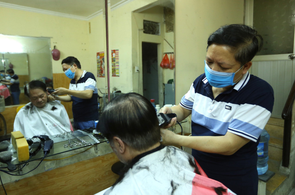 Anh Đào Quang Tiến (chủ tiệm cắt tóc thuộc phường Phạm Đình Hổ) luôn tay phục vụ khách hàng trong sáng mở cửa trở lại. (Ảnh: Hoàng Hiếu/TTXVN)