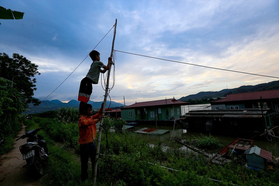Hai bố con đang kéo lại đường dây điện để thắp sáng khi thủy điện Hòa Bình mở cửa xả lũ đầu tiên ngày 12/6/2022 làm nước sông Đà dâng cao gây chia cắt các hộ và xảy ra các sự cố về dây điện tại làng vạn chài. (Ảnh: Trọng Đạt/TTXVN)