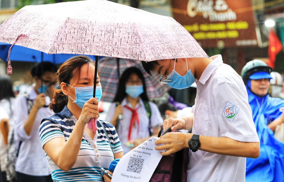 Hình ảnh những bậc cha mẹ đội mưa che ô đưa con đi thi kỳ thi tuyển sinh lớp 10 THPT 2021. (Ảnh: Thành Đạt/TTXVN)