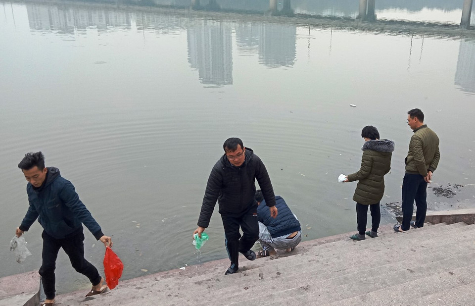 Sau khi thả cá tiễn Táo quân về trời, người dân cầm túi nilon lên vứt tại các điểm tập kết rác ven bờ. (Ảnh: Hùng Võ/Vietnam+)