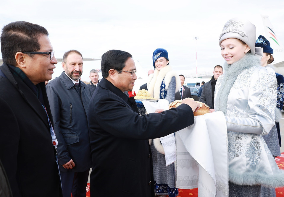 Thiếu nữ Nga trong trang phục truyền thống trân trọng mời Thủ tướng Phạm Minh Chính thưởng thức bánh mì chấm muối theo nghi thức đón khách quý của Nga. (Ảnh: Dương Giang/TTXVN)