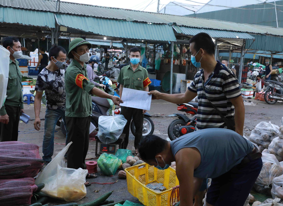 Lực lượng chức năng chợ đầu mối Minh Khai thường xuyên tuyên truyền, nhắc nhở người dân thực hiện nghiêm các quy định về phòng chống dịch. (Ảnh: Vũ Sinh/TTXVN)
