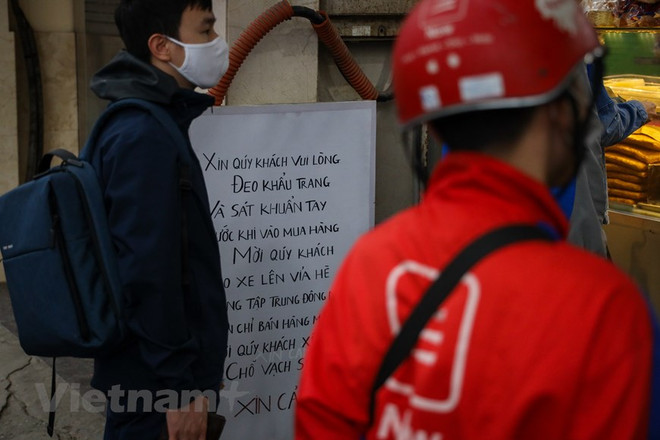 Cửa hàng này cũng treo biển khuyến cáo khách hàng đeo khẩu trang và sát khuẩn tay trước khi mua hàng. (Ảnh: Minh Sơn/Vietnam+) TP. HCM: Các điểm kinh doanh thực hiện tiêu chí an toàn khi mở cửa lại ảnh 1
