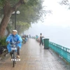 Người dân phải áo mưa vì trời xuất hiện mưa phùn, mưa nhỏ ở khu vực đường Thanh Niên và Hồ Tây. (Ảnh: Nguyễn Hoa/TTXVN phát)