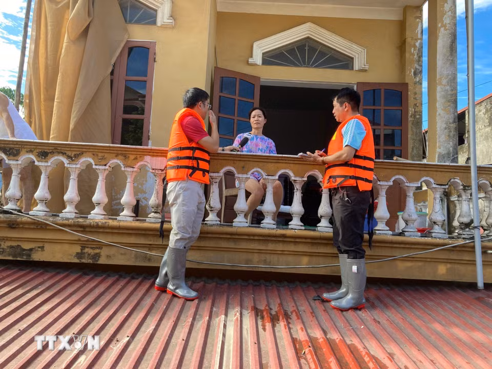 Phóng viên TTXVN đứng trên mái nhà phỏng vấn người dân về tình hình ứng phó với ngập lụt. (Ảnh: Thắng Trung/TTXVN)