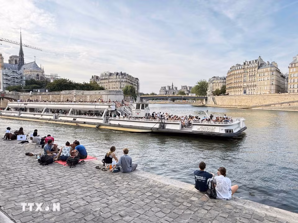 Người dân và du khách ngồi thư giãn bên bờ sông Seine, phía xa là Nhà thờ Đức Bà Paris. (Ảnh: Hữu Chiến/TTXVN)