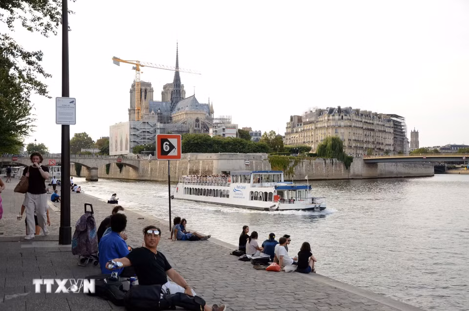 Người dân và du khách ngồi thư giãn bên bờ sông Seine, phía xa là Nhà thờ Đức Bà Paris. (Ảnh: Hữu Chiến/TTXVN)