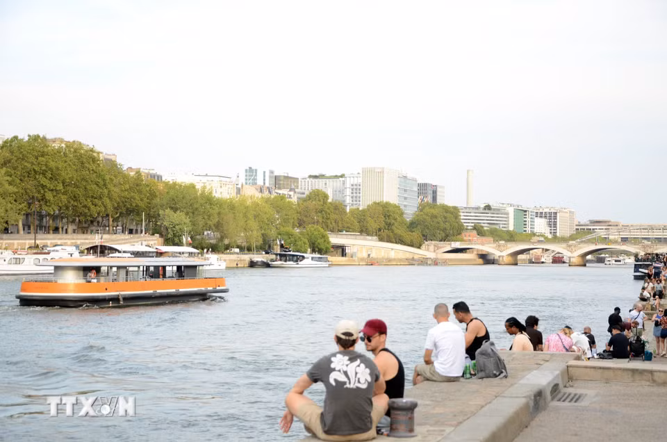 Người dân ngồi thư giãn sát mép nước, ngắm nhìn tàu thuyền chở du khách qua lại trên sông Seine. (Ảnh: Hữu Chiến /TTXVN)