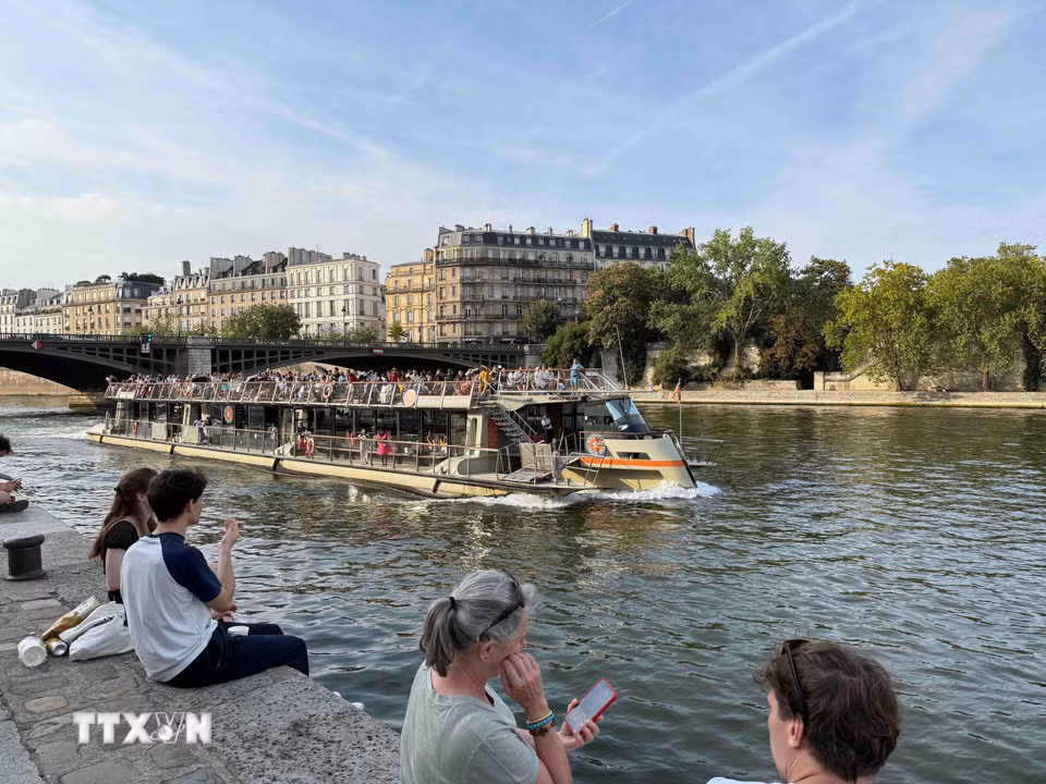 Tàu du lịch trên sông Seine đi qua những khu phố cổ của Paris, trong khi người dân ngồi nghỉ ngay sát mép nước. (Ảnh: Hữu Chiến/TTXVN)
