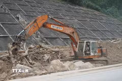 Đơn vị thi công phải dùng xe máy chuyên dụng để phá các tảng đá lớn nặng hàng chục tấn bị nước lũ cuốn lăn xuống đường. (Ảnh: Quốc Dũng/TTXVN)