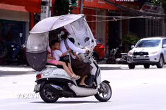 Giữa đỉnh điểm nắng nóng mùa hè, nhiều người dân lắp thêm mái che chống nắng cho xe máy khi chở trẻ nhỏ di chuyển trên đường phố tỉnh Phú Thọ. (Ảnh: Hoàng Hùng/TTXVN)