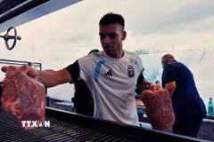 Lautaro Martínez phụ giúp đặt các miếng thịt lên vỉ nướng trong bữa tiệc asado của đội tuyển Argentina. (Ảnh: Infobae)