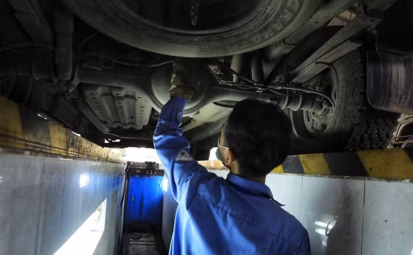 Kiểm định viên kiểm tra gầm bệ phương tiện giao thông. (Ảnh: Tuấn Anh/TTXVN)