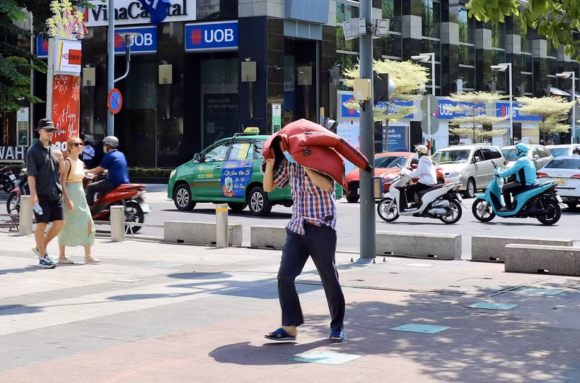 Một người dân tại Thành phố Hồ Chí Minh dùng áo che kín đầu, bước vội giữa trời nắng nóng. (Ảnh: Hồng Giang/TTXVN)